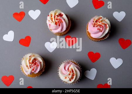 Parsemez de petits gâteaux frais au milieu de formes de coeur blanc et rouge sur fond gris Banque D'Images