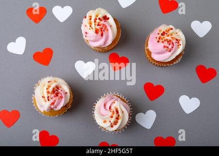 Parsemez de petits gâteaux frais au milieu de formes rouges et blanches de coeur sur fond gris Banque D'Images