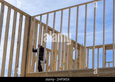 Vue aérienne du dessus d'un travailleur avec des gants de protection blancs tenant une planche l'installant sur une construction domestique à l'aide d'un marteau pneumatique dans des poutres en bois cloueuses. Banque D'Images