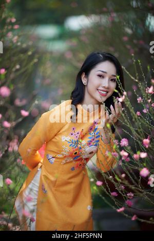 Ho Chi Minh ville, Vietnam: Fille vietnamienne portant ao dai posant avec des fleurs de pêche pour célébrer la nouvelle année Banque D'Images