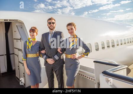 Un capitaine d'aviation masculin et deux préposés de vol féminins regardant la caméra et souriant en se tenant près des portes de l'avion Banque D'Images