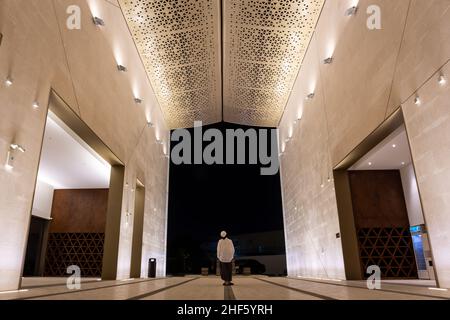 Cour illuminée de la Mosquée de la lumière à Dubaï avec une femme musulmane debout au milieu, façade et toit avec des motifs géométriques triangulaires. Banque D'Images