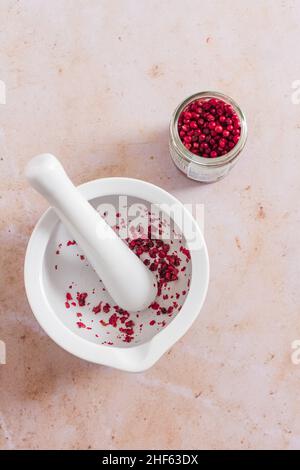 Pilon blanc et mortier avec grains de poivre rose moulu. Banque D'Images