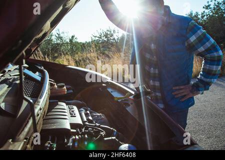 L'homme ouvre le capot de la voiture en panne sur le côté de la route.Assistance routière. Banque D'Images