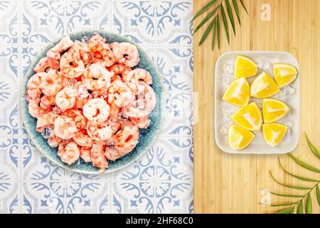 Cuisson des crevettes.Composition alimentaire avec crevettes pillées congelées avec glaçons sur une assiette bleue et tranches de citron dans une cuisine écologique.Méditerranée, Banque D'Images