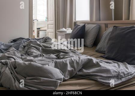 Un lit non fait avec deux couettes en duvet grises.Concept du matin Banque D'Images