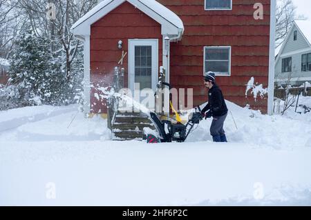 un jeune homme nettoie la cour avec un souffleur de neige après la tempête de neige Banque D'Images