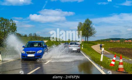 Une eau stagnante en allemagne, une menace mondiale causée par le réchauffement climatique.Une voiture éclabousse la haute eau, conduisant sur une rade inondée Banque D'Images