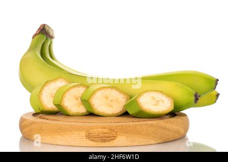 Une moitié et quatre tranches de banane verte biologique sur une planche à découper en bois, en gros plan, isolée sur du blanc. Banque D'Images