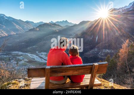 Deux personnes (père et fille) assis sur un banc en automne, regardant le coucher du soleil, Agordo, province de Belluno, Vénétie, Italie Banque D'Images