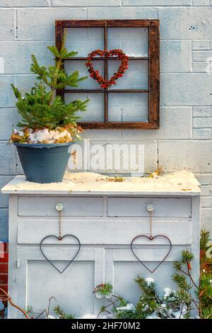 Baies rouges accrochées autour d'un coeur en fil de fer accroché à un cadre rustique de fenêtre en bois vintage.La décoration de la Saint-Valentin est sur un mur de briques blanches et une table. Banque D'Images