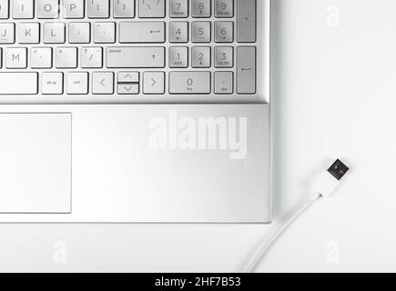 Ordinateur portable et câble USB blanc sur le bureau. Banque D'Images