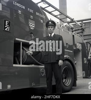 1960s, historique, un officier de station de la brigade des pompiers de Londres debout dans son uniforme par un moteur d'incendie Dennis à la caserne des pompiers de Lewisham, sud-est de Londres, Angleterre, Royaume-Uni.Les frères Dennis, John et Raymond, ont commencé à fabriquer et à vendre des bicyclettes en 1895, avant de progresser vers les voitures et les véhicules commerciaux et le légendaire moteur d'incendie. Banque D'Images