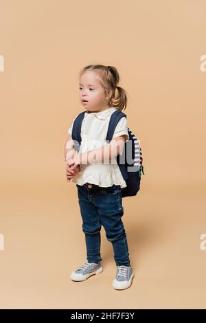 fille avec le syndrome de down debout avec sac à dos sur beige Banque D'Images