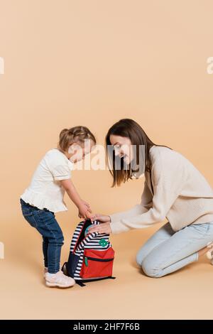 fille avec le syndrome de down et mère excitée regardant le sac à dos sur beige Banque D'Images