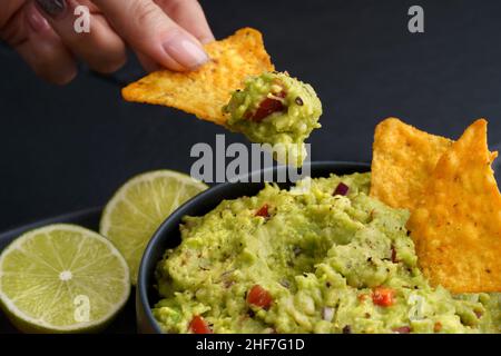 Femme tenant main puce de tortilla ou nachos avec savoureux guacamole trempée sur un fond noir Banque D'Images