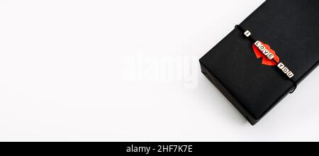 Emballage cadeau de la Saint-Valentin, forfait.Toile de fond cadeau de la Saint-Valentin avec boîte-cadeau d'artisanat noir avec texte I Love You et deux coeurs en papier rouge. Banque D'Images