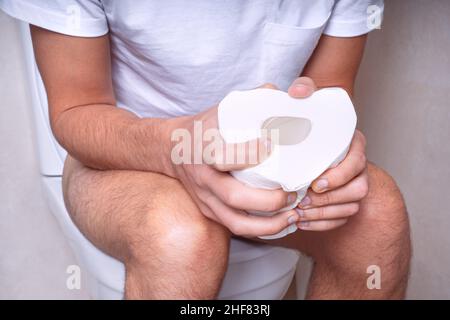 Homme assis sur les toilettes avec du papier toilette et souffrant de constipation, de diarrhée, de maux d'estomac ou de crampes Banque D'Images