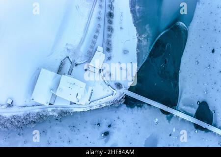 Italie, province de Belluno, Auronzo di Cadore, Dolomites, vue aérienne de quelques maisons et un pont à pied sur le lac de Santa Caterina, surface glacée avec des signes graphiques sur la glace Banque D'Images