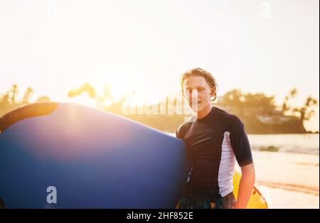 Portrait d'un jeune garçon avec des bretelles dentaires avec planche de surf va pour le surf.Il sourit et marche dans l'eau.Bonne enfance et vacances actives Banque D'Images