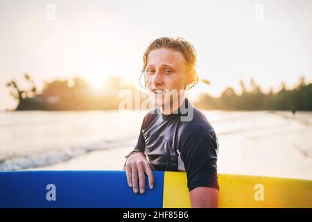 Portrait d'un jeune garçon avec des bretelles dentaires avec planche de surf va pour le surf.Il sourit et marche dans l'eau.Bonne enfance et vacances actives Banque D'Images