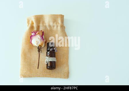 Plat de bouteille d'huile essentielle avec rose séchée sur un sac fait à la main sur fond blanc Banque D'Images