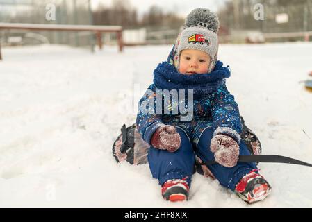 un petit garçon s'assoit sur un tubing dans une glissade enneigée en hiver Banque D'Images