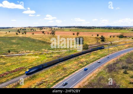 Train de voyageurs sur le chemin de fer dans le centre-ouest australien près de l'autoroute avec des voitures et des fermes agricoles. Banque D'Images