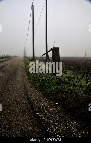 Route de campagne avec une ligne électrique tête et un bar à côté de lui lors d'une journée brumeuse dans la campagne italienne en hiver Banque D'Images