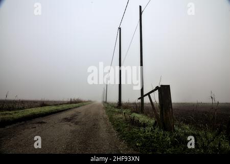 Route de campagne avec une ligne électrique tête et un bar à côté de lui lors d'une journée brumeuse dans la campagne italienne en hiver Banque D'Images