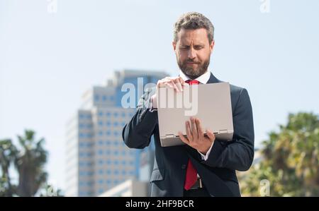homme d'affaires barbu en tenue de cérémonie travaillant sur ordinateur à l'extérieur du bureau, entreprise agile Banque D'Images