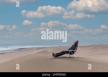 Homme adulte couché sur une chaise longue de plage en face de la mer Banque D'Images