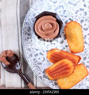 Top vue sur la Madeleine sur un plateau rustique, petit cookie français traditionnel fait maison avec une coque sur fond rustique.Servi avec de la sauce au chocolat Banque D'Images