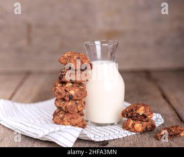 Croustilles au chocolat maison empilées biscuits aux noix de macadamia, servis avec une bouteille de lait.Espace de copie pour le texte, la recette ou la publicité sur la rouille en bois Banque D'Images