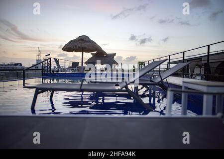 Vue stupéfiante de la piscine peu profonde et des lits de plage avec coucher de soleil comme arrière-plan Banque D'Images