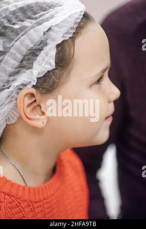 Portrait en gros plan en profil du visage de la petite fille dans la casquette médicale jetable en attente de procédures médicales à l'hôpital. Banque D'Images