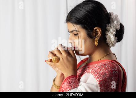 Une belle femme indienne en saree rouge soufflant conch shell sur fond blanc Banque D'Images