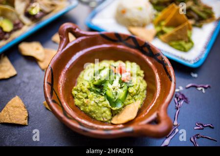 Délicieux guacamole épicé dans un pot d'argile traditionnel au-dessus de la surface sombre Banque D'Images