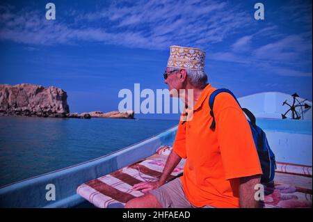 Touriste senior avec chapeau d'Oman assis sur le bateau et naviguant le long de la côte Banque D'Images