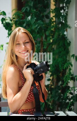 Bonne jeune femme caucasienne, millénaire ou génération z avec un long brunette tenant la caméra dans la main dans un café extérieur moderne.Hipster Influencer utilisant les réseaux sociaux. Banque D'Images