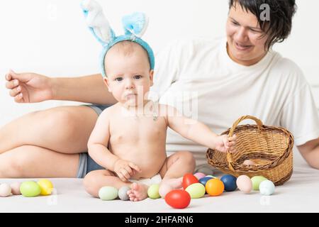 Maman et bébé avec des oreilles de lapin, avec des œufs de Pâques dans leurs mains, assis sur le canapé, parents et enfants jouent à l'intérieur. La famille fête Pâques Banque D'Images