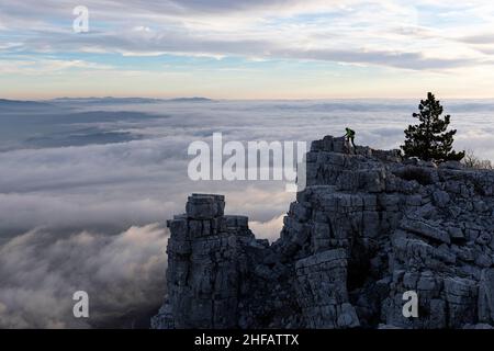 Homme grimpant sur la formation rocheuse avec le beau panorama de la vallée de Vipava en Slovénie, au coucher du soleil, en regardant du sommet de la montagne de Caven Banque D'Images