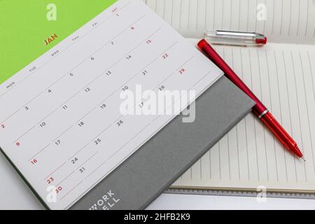 Calendrier de janvier 2022 avec page vierge de cahier et stylo rouge sur un bureau blanc Banque D'Images