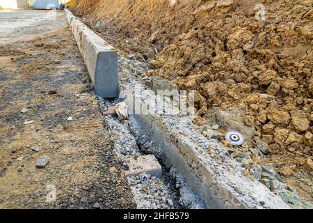Installation d'une pierre à affûter le long du bord d'une nouvelle route, dans une zone résidentielle en construction, attention sélective Banque D'Images