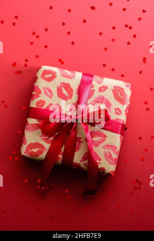 Boîte-cadeau papier artisanal avec marques rouges à lèvres, ruban rouge attaché sur fond rouge, vue du dessus.Joyeux cadeau de la Saint Valentin. Banque D'Images