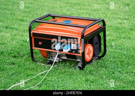 Générateur électrique portable avec fils électriques blancs connectés à lui sur l'herbe verte en plein air de jour d'été.Le générateur fournit un circuit électrique Banque D'Images