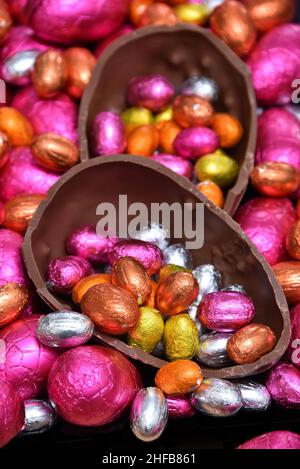 Pile de différentes tailles d'oeufs de pâques au chocolat enveloppés de feuilles colorées en rose, rouge, or, argent et orange avec deux moitiés d'un oeuf de chocolat. Banque D'Images