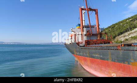 Antenne pour barge rouge, vide amarré le long de la rive de la mer près d'une pente couverte d'arbres verts sur fond bleu ciel.Gros plan pour un gros cargo dans un Banque D'Images