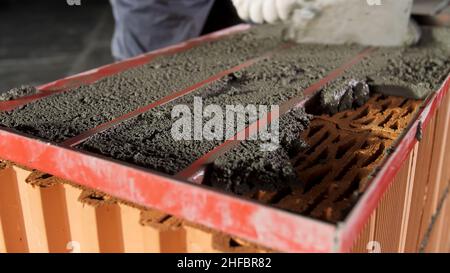 Ouvrier de construction utilisant la truelle pour niveler le mortier brut pour la fixation des couches de brique.Gros plan du ciment mis sur des briques rouges. Banque D'Images