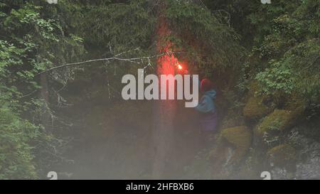 Homme explorer se tenant parmi les arbres verts et tenant feu rouge flamant de l'éclat d'être trouvé par quelqu'un.Perdu dans la nature sauvage et à la recherche de l'aide conc Banque D'Images